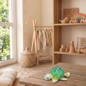Zöld színű, kézzel készített horgolt fidget teknős mintás fa asztalon, skandináv gyerekszoba háttérrel.